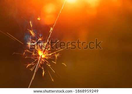 Burning sparkler in hand on background of christmas tree with lights in dark festive room. Young female celebrating new year with firework. Happy New Year