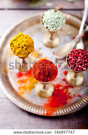 Various Indian spices in vintage metal cups on a metal tray on a wooden background