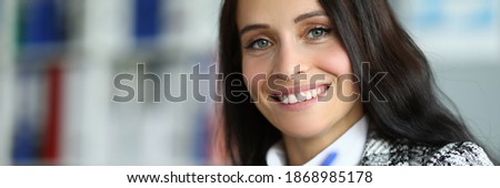 Close-up of cheerful pretty young woman smiling on camera. Lovely brunette lady signing document in company office. Good deal and success. Business and woman boss concept