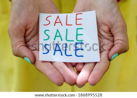 Text of the word sale in three different colors on paper in the hands of a young woman