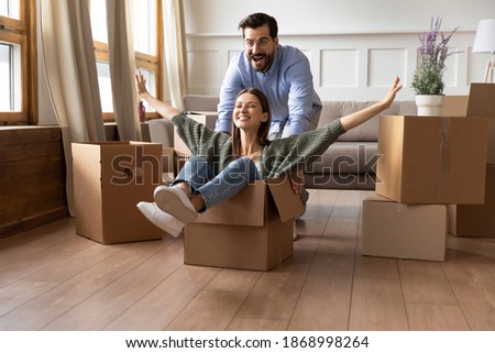 Overjoyed couple renters have fun ride in cardboard box relocate at new home together. Happy man and woman tenants engaged in funny activity feel playful on moving day. Relocation, rental concept. Royalty-Free Stock Photo #1868998264