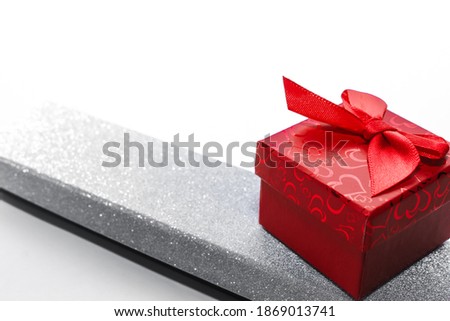 two gift boxes for ring, necklace and other jewelry on white background. long shiny silver box and square red box with red ribbon. holiday surprise. copy space.