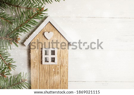 Model of a wooden house on a white wooden background and a natural spruce branch.