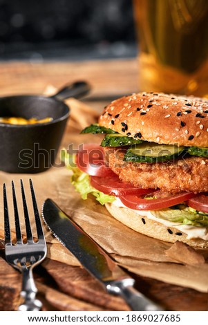 The concept of American fast food. A juicy American burger with two beef patties and a dark beer on a glass table and an orange background. Copy space