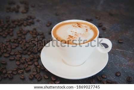 close up image of a cup of cappuccino coffee Italian style on dark tabletop decorated with roasted coffee beans , good for background with copy space.