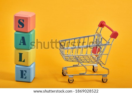 A miniature shopping cart and multi-colored cubes on yellow background. Sales word written on cubes.