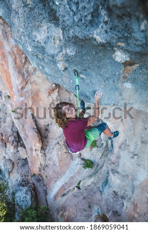 A young athlete climbs a rock, a climber trains on natural terrain, a man trains strength and endurance, rock climbing for children and teenagers, Young athlete hangs on a rope on a rock.