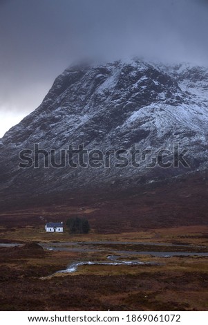 low mountain cabin in Glencoe, Scotland, Uk. typical highland building with snowy mountain Stob Dearg in the background. Snowy atmosphere in winter, after a big storm