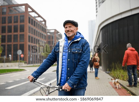 Happy senior man with bicycle outdoors on street in city, walking.
