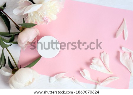 Delicate peonies with body care cream, top view, close-up, space for text
