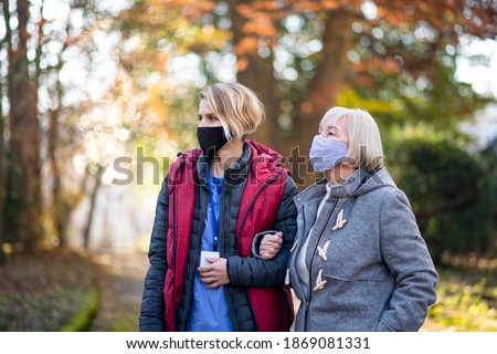 Senior woman with caregiver outdoors on a walk in park, coronavirus concept.