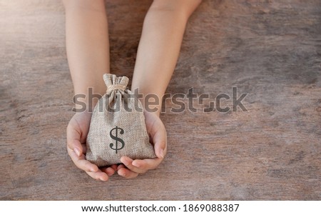 Child hand with bag of coins and copy space using as background concept to saving money, home loan, education plan for the future, retirement on wood table.