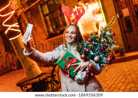 Smiling woman taking a selfie in the middle of the street with Christmas decorations. Young woman after christmas shopping. Christmas concept