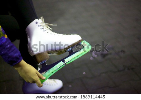 Hands take off the green plastic cover from the skate blade on the white leather shoe of a modern skate. Close-up



