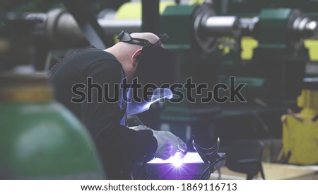 professional weld worker while using TIG Welding, wearing safety protective mask in selective focus view. Gas tungsten arc welding GTAW torch welder background.