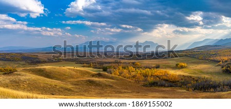 Vast prairie and forest in beautiful autumn. Sunlight passing blue sky and clouds on mountains. Fall color landscape background. Waterton Scenic Spot, Waterton Lakes National Park, Alberta, Canada. Royalty-Free Stock Photo #1869155002