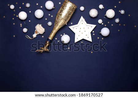 Christmas banner with white decor and golden champagne on navy blue background. New year celebration concept with balls, luminous star and bottle cap with had of deer