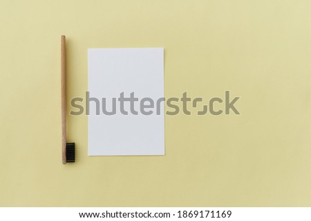 An empty paper sheet card with a model copy space and a wooden toothbrush, on a yellow background.
Minimum business brand template zero waste. Top View