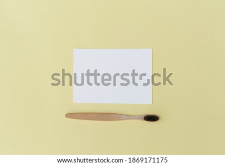 An empty paper sheet card with a model copy space and a wooden toothbrush, on a yellow background.
Minimum business brand template zero waste. Top View