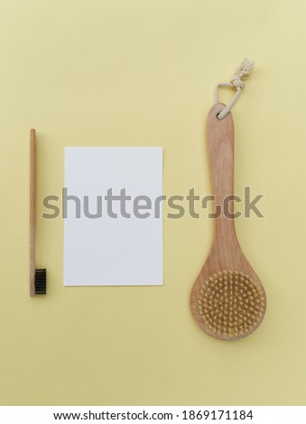 An empty paper sheet card with a model of copying space and a wooden toothbrush and a body brush, on a yellow background.
Minimum business brand template zero waste. Top View