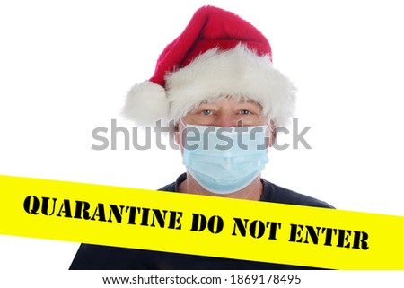 Coronavirus Quarantine Do Not Enter Caution Tape. A man wears a Santa Hat and a Medical Face Mask to help avoid contracting Coronavirus while behind Yellow Coronavirus Quarantine Caution Tape.  