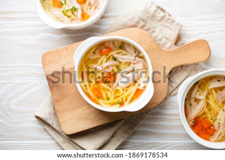 Warm healthy homemade chicken soup in white ceramic bowls on cutting board, white wooden table background. Traditional tasty chicken soup great for health and immune system. Top view