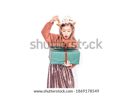 Child holding a box in green packaging with a gift. Christmas mood. She has antlers on her head.