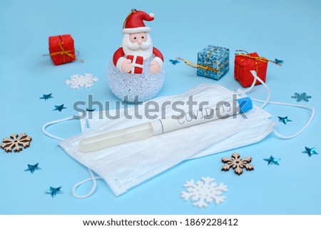 Close-up figure of santa claus and medical masks on a background of snowflakes and gift boxes on a blue background. Covid and New Year 2021