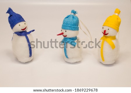 three christmas toys snowman two with red noses one without a nose in a yellow, blue, purple hat and scarves isolated on a white background