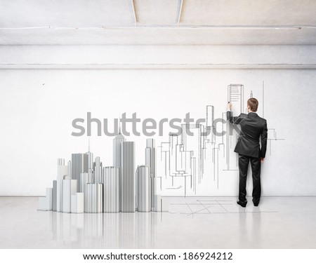 Man drawing city on a wall. Model of a city on a floor.