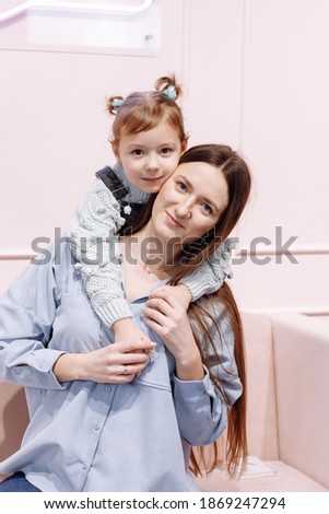 Happy loving family. young Mother and her little daughter are hugging and looking in camera on pink sofa and wall background. happy mother's, baby's day