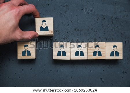 Wooden cubes with icons of men and an icon of women. Hand pulls out a cube with a woman icon. Concept of discrimination against women at work, lack of equality.