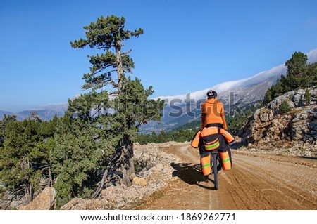 Athletic man in bright clothes rides a mountain bike with a huge cycling backpack on a dirt road through a pass in turkey