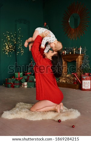Mother tossing up her little son sitting on the floor against the backdrop of a Christmas tree.