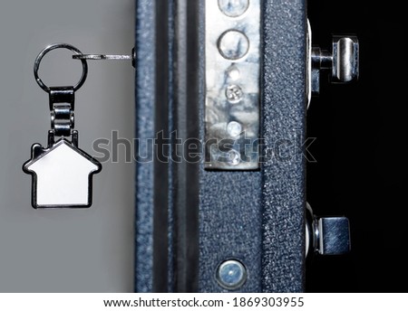 Key with metal trinket in the door lock. The door is half open. Blurred background. Real estate for rent.