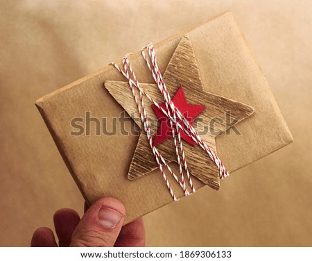 male hand holding gift box wrapped in craft paper. wooden star and branches of pine. happy new 2021 year. merry christmas.