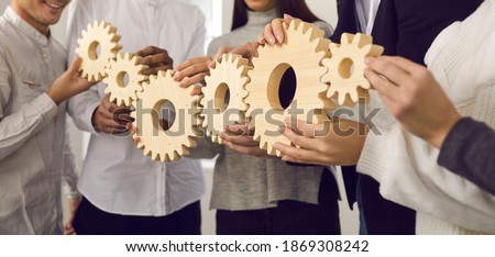Team of young people making gear chain as metaphor for collaboration, coordinated group work, teamwork, professional interaction, building strong company and effective well-functioning business system Royalty-Free Stock Photo #1869308242