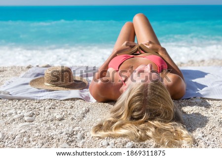 Woman holding a book while lying on her back over a towel on a sunny beach.