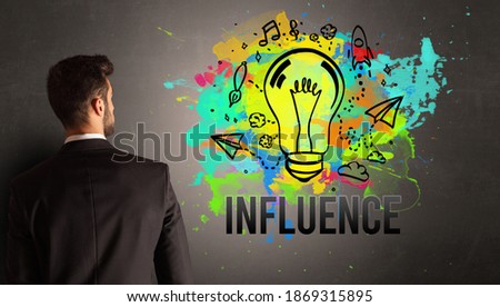 businessman drawing colorful light bulb with INFLUENCE inscription on textured concrete wall, new business idea concept