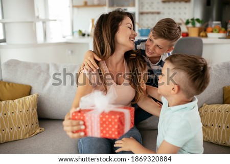 Two young sons are giving their mother a gift. Mother is suprised to receive a present from sons.