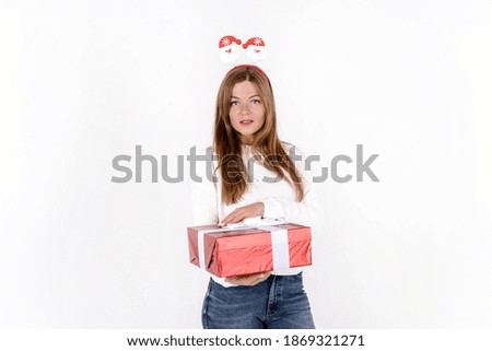 Photo of an excited young woman wearing christmas head hoop and holding christmas gift isolated over grey background