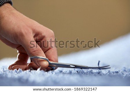 Closeup of hand cutting off string on a carpet with scissors. Carpet cleaning service Royalty-Free Stock Photo #1869322147