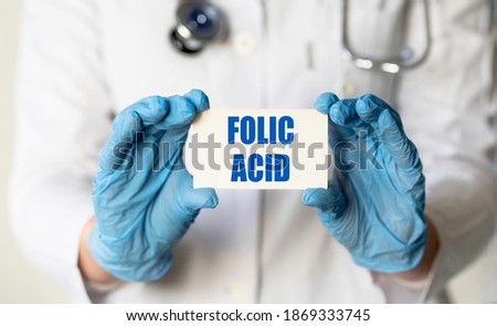 A medical worker in gloves holds a card with the words FOLIC ACID. Medical concept.