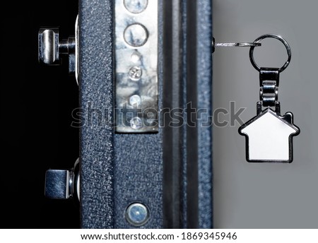 Key with metal trinket in the door lock. The door is half open. Blurred background. Real estate for rent.