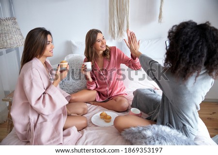 Best friends giving five to each other while eating cupcakes at the bed on the pajamas party. Stock photo