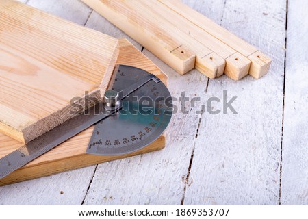 A carpenter's protractor placed on a piece of wood. Measurement of the kata in a carpentry workshop. Light background.