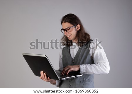 Programming and writing code, developing software products. Geek guy, with long hair and glasses, holding a laptop, gray background