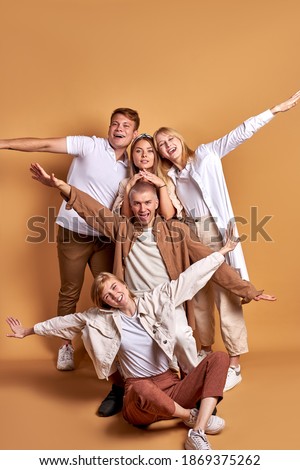 portrait of happy smiling group of youth posing together, wearing trendy coats shirts, casual clothes. friendly men and women isolated over brown studio background