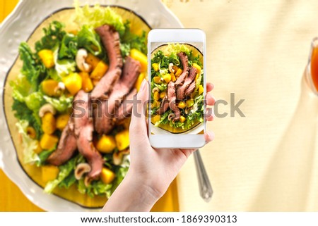 Hand taking a photo of Healthy food with smartphone. Woman using phone mobile apps make digital picture on screen of diet nutrition Vegetarian salad on table, top view
