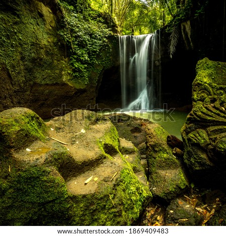 Beautiful waterfall in rainforest. Tropical landscape. Slow shutter speed, motion photography. Foreground with big stones. Environment concept. Travel and adventure. Suwat waterfall, Bali, Indonesia
